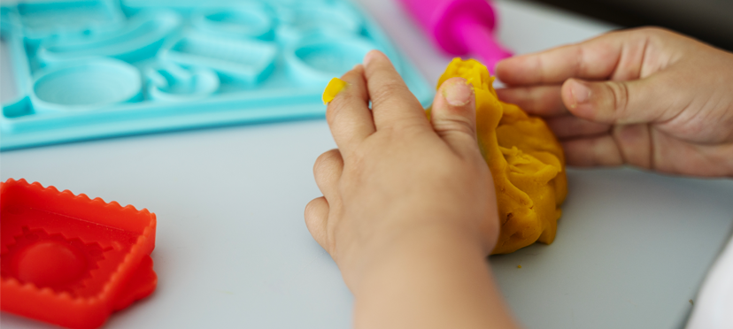 Enfant utilisant des pinces pour manipuler des perles, ou jouant avec de la pâte à modeler sous supervision.