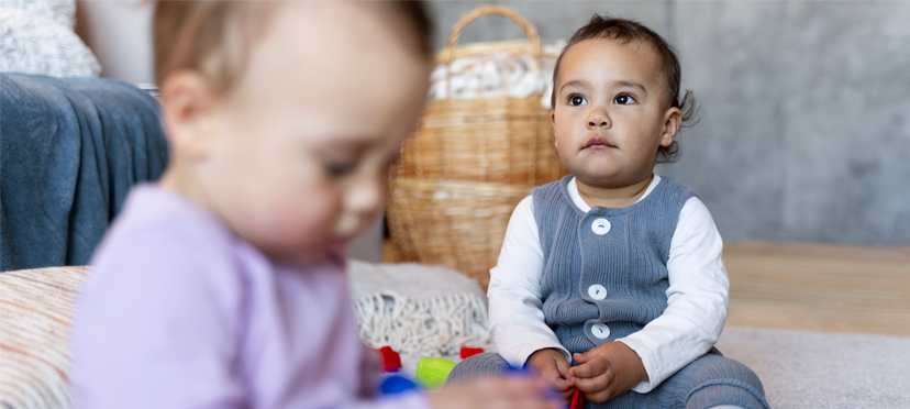 Deux enfants jouant côte à côte et partageant des jouets, sous la supervision d’une éducatrice attentive.