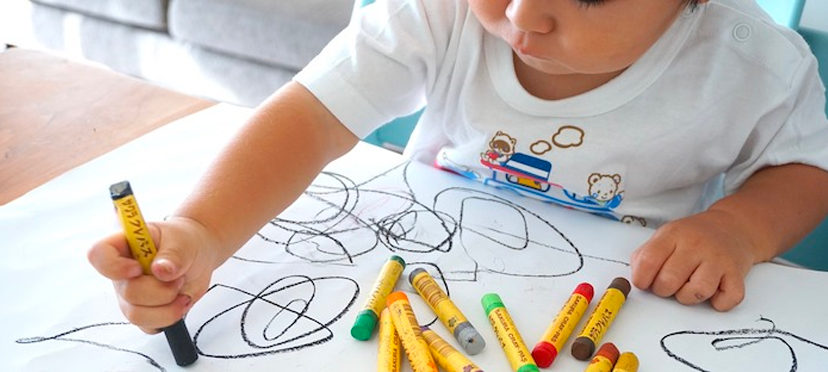 Enfant de 18 mois dessinant avec des feutres lavables sur une feuille blanche sous la supervision bienveillante d'une éducatrice.