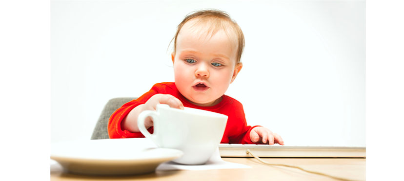 Bébé cherchant des céréales sous une tasse colorée, concentré sur le développement de ses compétences de mémoire et d'attention.