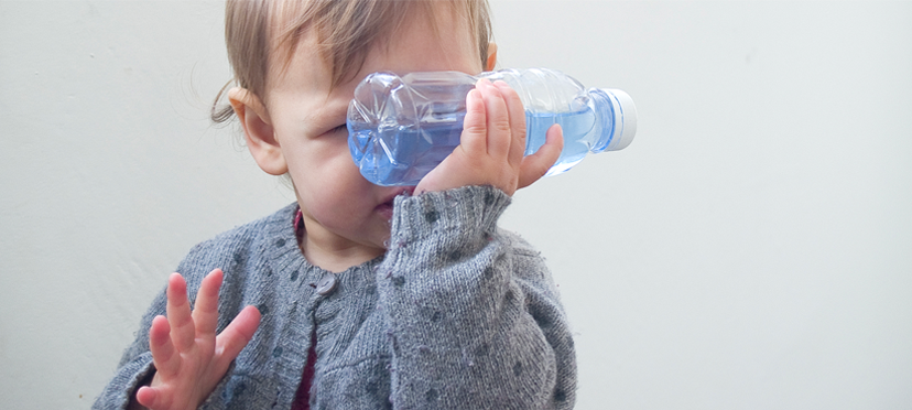 Bébé tenant une bouteille avec du riz coloré, explorant les sons et développant sa motricité fine.