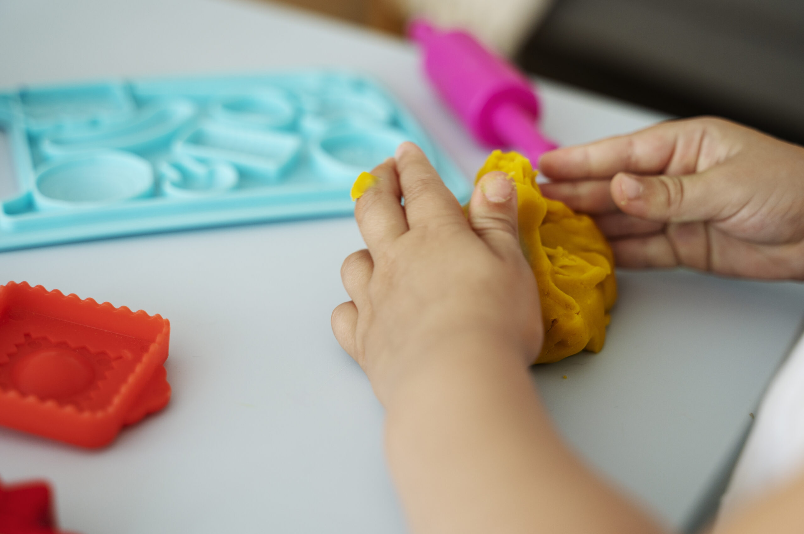 Enfant utilisant des pinces pour manipuler des perles, ou jouant avec de la pâte à modeler sous supervision.